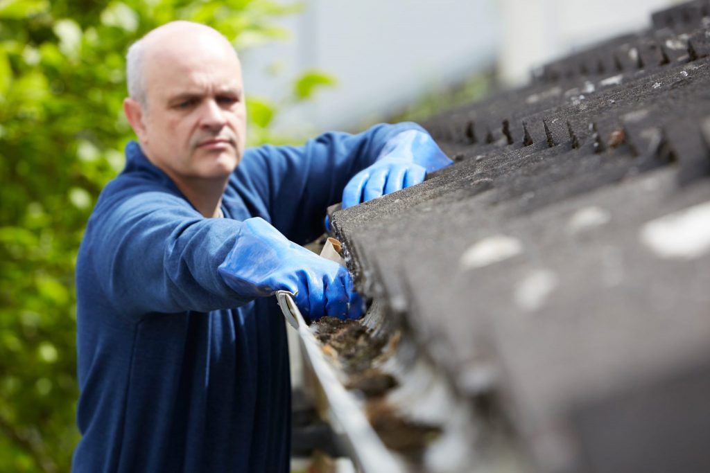 Man with gloves cleaning out gutter